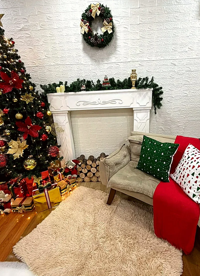 Cenário da sala: árvore de Natal iluminada com presentes, lareira branca com guirlanda e poltrona com almofadas natalinas