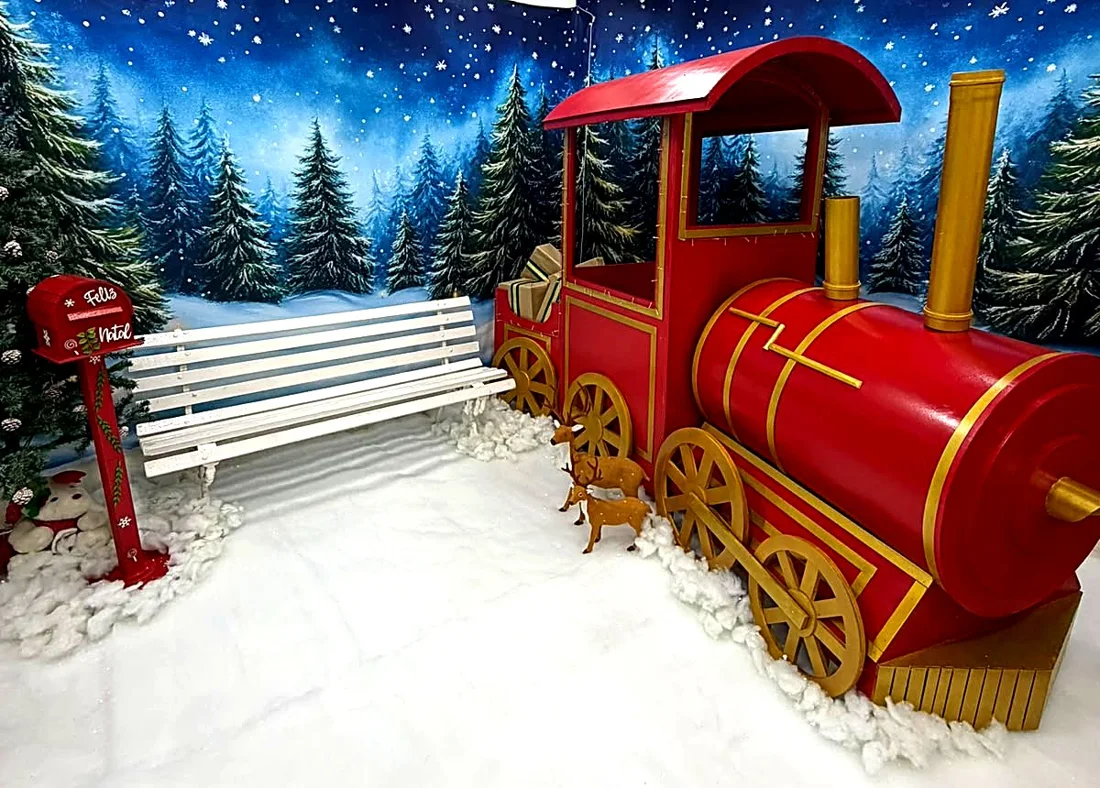 Cenário do trem no estúdio: locomotiva vermelha e dourada, banco branco e caixa de correio do Papai Noel sobre neve, com painel de floresta noturna ao fundo